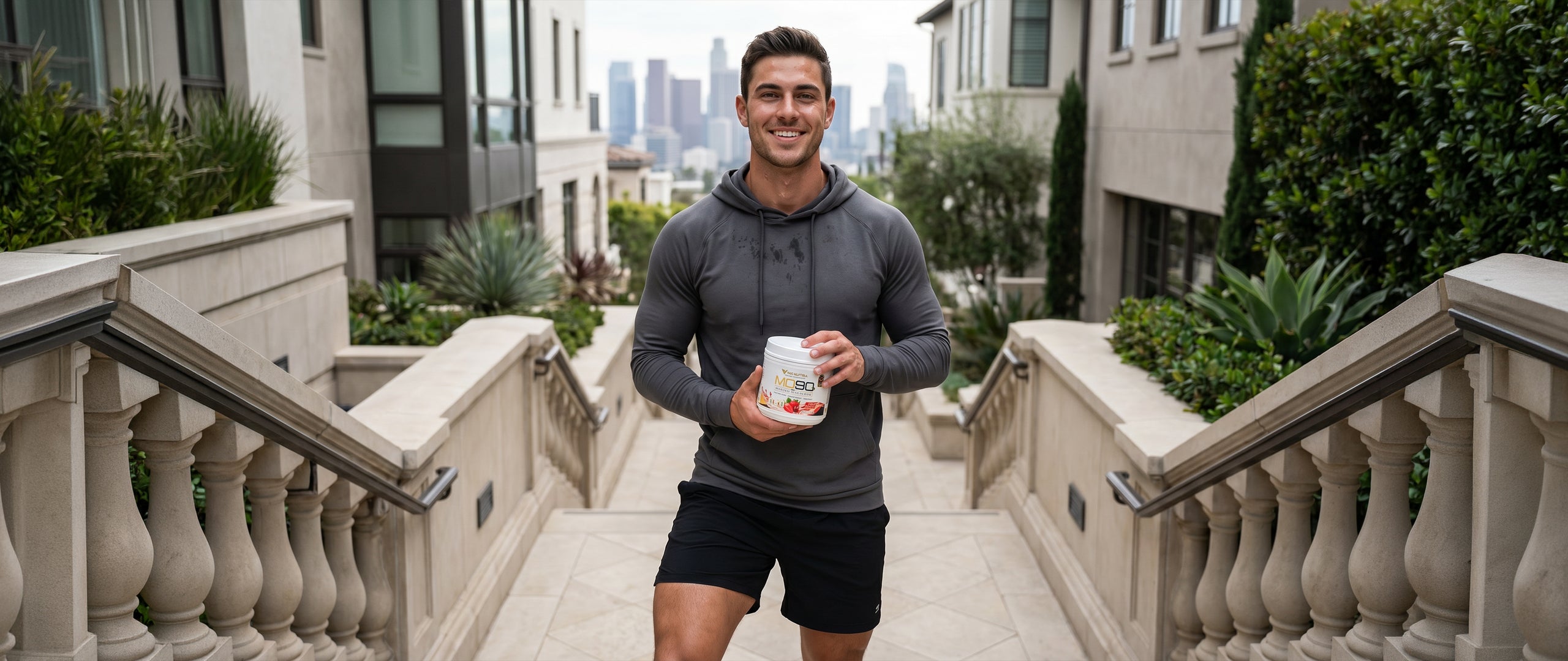 Fit man holding NG Nutra's MO90 2.0 - Muscle Overload on a staircase with a cityscape background.